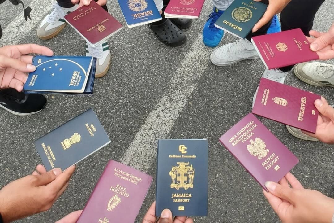 Hands from many nations holding their passports together in a circle.