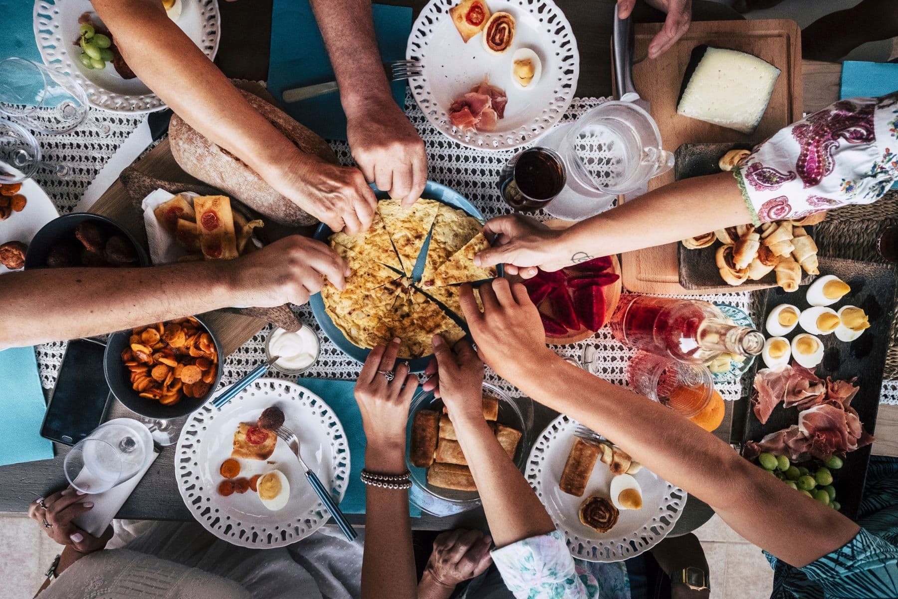 Hands reaching together over a shared table of food.