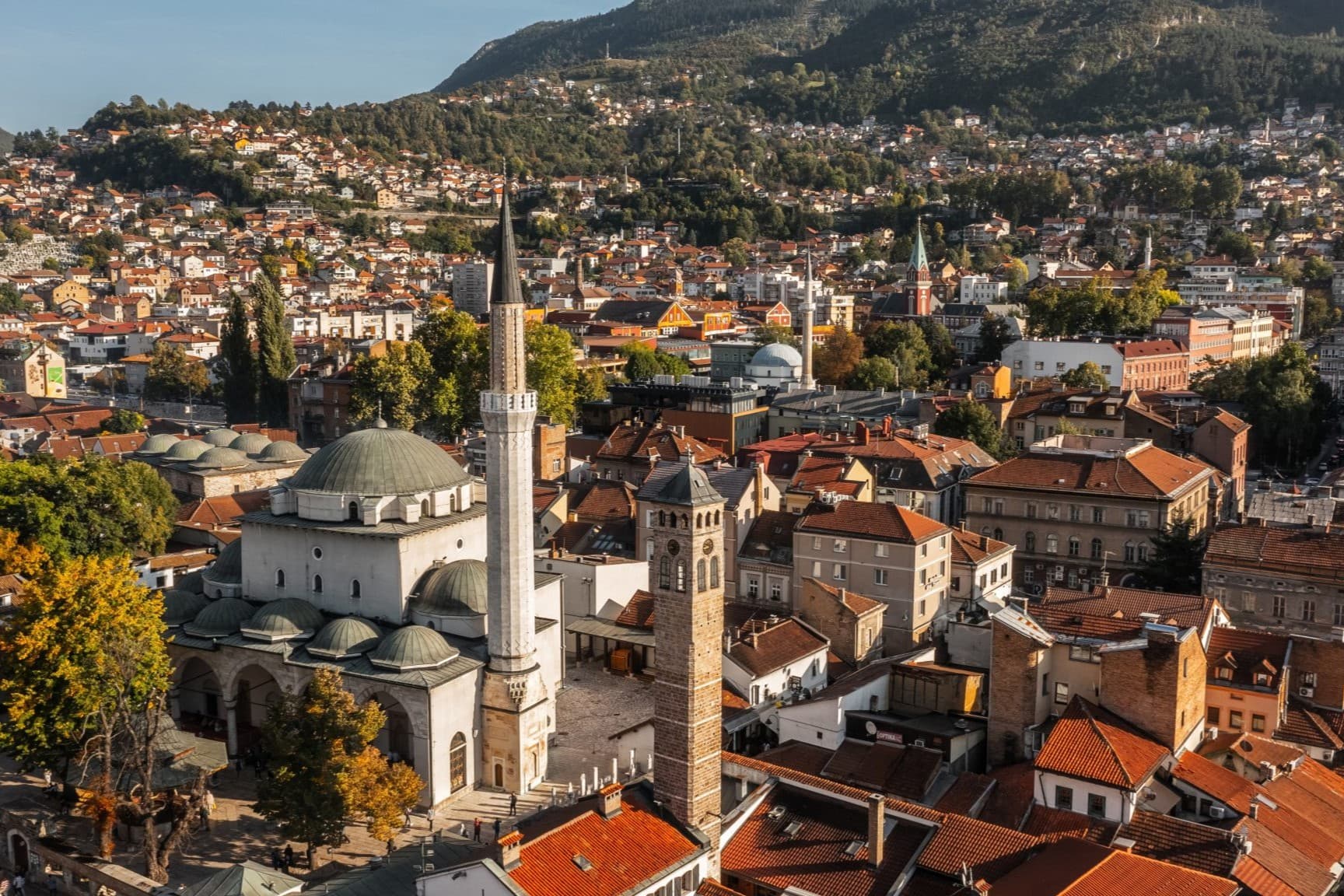 An elevated view over Sarajevo's old town, with the Gazi Husrev-beg Mosque and the Sahat Kula clock tower among the rooftops.